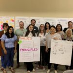 A group of smiling people holding up poster paper with "VALUES" and "PRINCIPLES" written on it, from a participatory design workshop